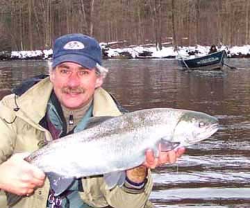 Salmon River Fishing Report Guide displays a nice Steelhead with his drift boat in back ground on the Salmon River in Pulaski NY.